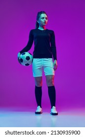 Portrait Of Beautiful Girl, Professional Female Soccer Player With Football Ball Isolated On Purple Background In Neon. Concept Of Sport, Fitness. Young Spotive Girl In Black And White Football Kit