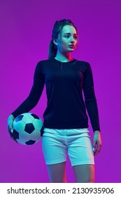 Portrait Of Beautiful Girl, Professional Female Soccer Player With Football Ball Isolated On Purple Background In Neon. Concept Of Sport, Fitness. Young Spotive Girl In Black And White Football Kit