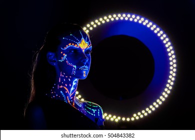 Portrait of beautiful girl with ultraviolet paint on her face. Girl with neon make-up in color light.