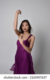 Portrait Of Beautiful Girl Wearing Flowing Fantasy Purple Ball Gown. Standing With Gestural Hand Poses, Fro Ma Low Angle Perspective Isolated On Studio Background.