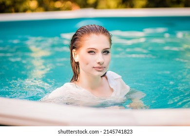 Portrait Of A Beautiful Girl With Wet Hair Floating In The Pool, Wearing A White Shirt. Rest In The Water In Hot Weather.
