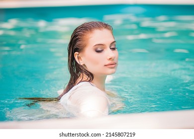 Portrait Of A Beautiful Girl With Wet Hair Floating In The Pool, Wearing A White Shirt. Rest In The Water In Hot Weather.
