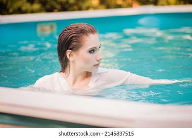 Portrait Of A Beautiful Girl With Wet Hair Floating In The Pool, Wearing A White Shirt. Rest In The Water In Hot Weather.
