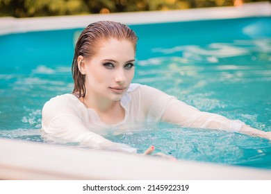 Portrait Of A Beautiful Girl With Wet Hair Floating In The Pool, Wearing A White Shirt. Rest In The Water In Hot Weather.
