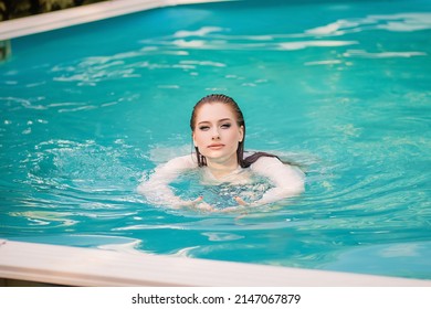 Portrait Of A Beautiful Girl With Wet Hair Floating In The Pool, Wearing A White Shirt. Rest In The Water In Hot Weather.
