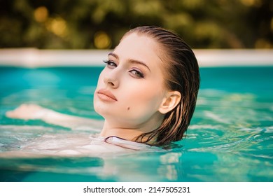 Portrait Of A Beautiful Girl With Wet Hair Floating In The Pool, Wearing A White Shirt. Rest In The Water In Hot Weather.
