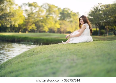 Portrait of a beautiful girl in white dress, sitting on the grass field at the river side