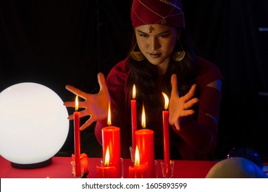 Portrait of Beautiful Gypsy fortune teller woman smile while hands around the red candles and looking. Divine magic, Forecast esoteric astrology supernaturalism, magical power, alchemy concept. - Shutterstock ID 1605893599
