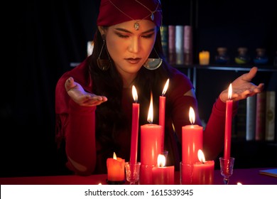 Portrait of Beautiful Gypsy fortune teller woman Casting a spell while hands around the red candles. Divine magic, Forecast esoteric astrology supernaturalism, magical power, alchemy concept. - Shutterstock ID 1615339345