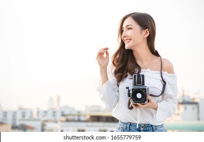 Portrait beautiful happy asian woman photographer in fashion look taking photo. Pretty cool young woman model  retro film vintage camera curly hair outdoors over rooftop sky solo traveler copy space - Powered by Shutterstock