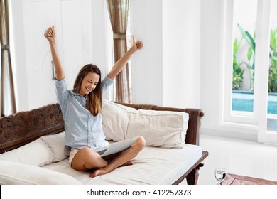 Portrait Of Beautiful Happy Smiling Woman Cheering And Celebrating Successful Business Deal While  Using Laptop Computer At Home. Female Celebrating Victory With Arms Up. Success, Winning Concept
