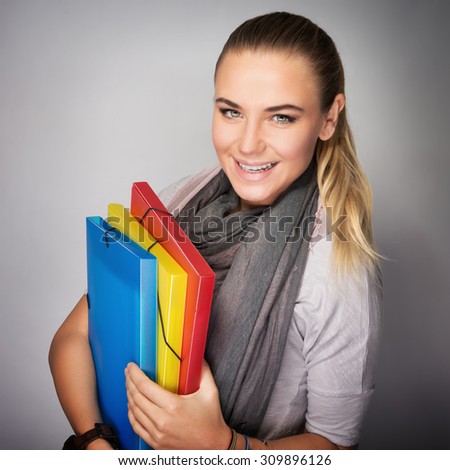 Portrait of beautiful happy student girl with colorful folders in hands over gray background, enjoying start of educational season