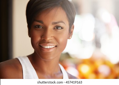 Portrait of beautiful happy young black model with short pixie hairstyle and healthy clean skin looking and smiling at the camera with cheerful expression, showing her white teeth, posing outdoors