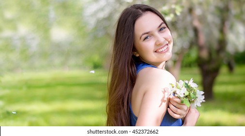 Portrait beautiful happy young woman enjoying smell in a flowering spring garden
natural girl without makeup