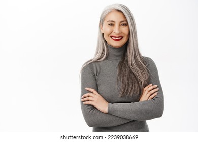 Portrait of beautiful, healthy smiling middle aged asian woman, cross arms on chest, looking confident and happy, standing over white background - Shutterstock ID 2239038669