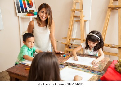 Portrait Of A Beautiful Hispanic Art Teacher And Her Students Drawing In Class And Having Fun