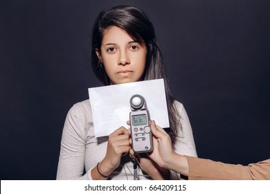 Portrait of beautiful hispanic latin brunette young woman in studio holding white paper and flash meter, measuring light, on plain black background - Powered by Shutterstock