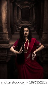 Portrait of beautiful Indian girl in heritage stepwell wearing traditional Indian red saree, gold jewellery and bangles holding religious plate. Maa Durga agomoni shoot concept