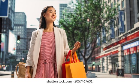 Portrait Of Beautiful Japanese Female Wearing Smart Casual Clothes On The Street. Successful Female Putting Shopping Bags On Her Shoulder In Big Urban City Environment Living The Urban Lifestyle.