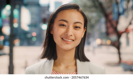 Portrait Of Beautiful Japanese Female Wearing Smart Casual Clothes Posing On The Street. Successful Female In Big City Living The Urban Lifestyle. Background With Office Buildings And Billboards.