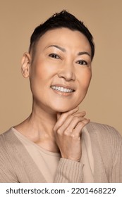 portrait of beautiful japanese woman in her 50s with alopecia smiling confidently posing and touching her face with her hand on neutral background Stock Photo