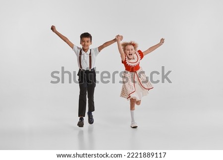 Portrait of beautiful little children, boy and girl in vintage clothes isolated over grey background. Back to school. Concept of childhood, creativity, retro vintage fashion, friendship, art