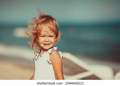 Portrait of a beautiful little girl looking at camera emotionally , wind blowing and moving her hair, hirl at sea beach