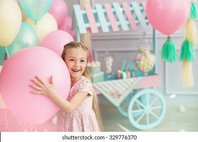 A portrait of a beautiful little girl smiles and holds in a hands a big color balloon in the studio with many balloons and a toy candy shop
