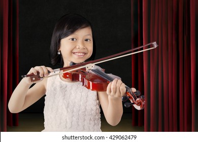 Portrait Of A Beautiful Little Girl Smiling At The Camera While Playing A Violin On The Stage