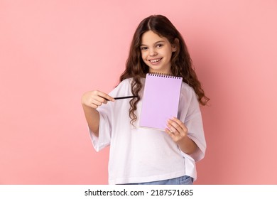 Portrait of beautiful little girl wearing white T-shirt pointing at paper notebook, looking smiling at camera, has positive expression. Indoor studio shot isolated on pink background. - Powered by Shutterstock