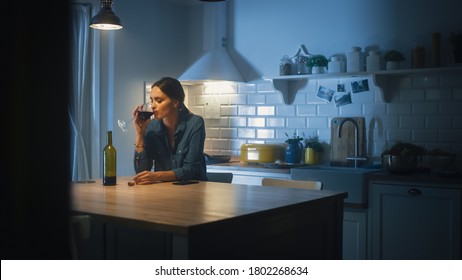 Portrait Of Beautiful Lonely Young Woman Drinking From A Wine Glass In The Dark Kitchen. Depressed And Sad Adult Girl With Alcohol Problem Drinks Alone, Bad Relationships, Work Stress, Other Problems