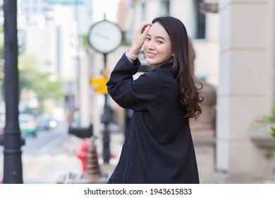 A Portrait Of A Beautiful, Long-haired Asian Woman In A Black Coat Walking And Smiling Happy Outdoors In The City.