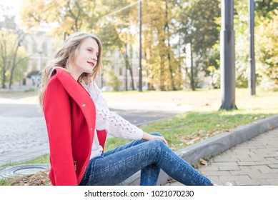 Portrait of beautiful long-haired girl in casual outfit leaning on fence in sunny park.