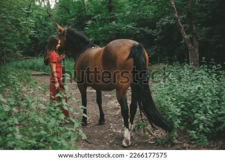 portrait of a beautiful long-haired girl in a red dress and a horse in a grove
