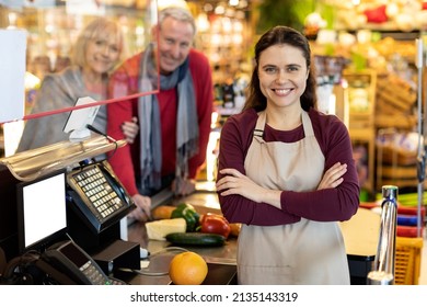 Portrait Of Beautiful Long-haired Young Woman Cashier Smiling At Camera At Workplace. Friendly Worker Assisting Cheerful Senior Couple At Cashdesk At Newest Supermarket. Good Service Concept