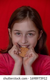 Portrait Of Beautiful, Lovely, L Child Girl, Bites Cookies On Red Background. Girl Eating Cookies. Girl 9 Years Old Portrait. The Concept Of Food And Man. Teenager