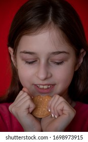 Portrait Of Beautiful, Lovely, L Child Girl, Bites Cookies On Red Background. Girl Eating Cookies. Girl 9 Years Old Portrait. The Concept Of Food And Man. Teenager