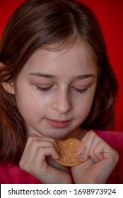 Portrait Of Beautiful, Lovely, L Child Girl, Bites Cookies On Red Background. Girl Eating Cookies. Girl 9 Years Old Portrait. The Concept Of Food And Man. Teenager