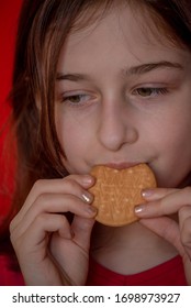 Portrait Of Beautiful, Lovely, L Child Girl, Bites Cookies On Red Background. Girl Eating Cookies. Girl 9 Years Old Portrait. The Concept Of Food And Man. Teenager