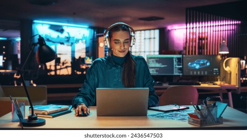 Portrait of a Beautiful Manager Sitting at a Desk in Creative Agency, Using Laptop Computer. Young Stylish Female with Headphones Looking at Camera with Big Smile While Working on New Project - Powered by Shutterstock