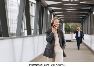 Portrait of a beautiful mature business woman in suit and gray jacket smiling and talking on the phone on a modern urban and office buildings background