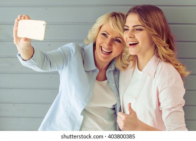 Portrait of beautiful mature mother and her daughter making a selfie using smart phone and smiling, against gray background