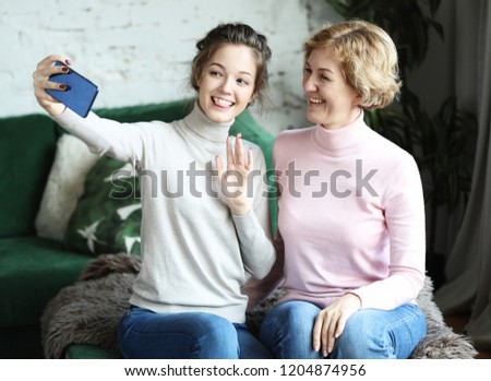 Portrait of beautiful mature mother and her daughter making a selfie using smart phone and smiling, home and happy.