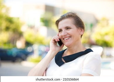 Portrait Beautiful Mature Woman Or Businesswoman In Her Forties Talking On A Cell Phone, Having Pleasant Conversation, Receiving Good News, Outdoors Background. Positive Facial Expressions