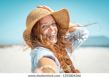 Portrait of beautiful mature woman in casual wearing straw hat at seaside. Cheerful young woman smiling at beach during summer vacation. Happy girl with red hair and freckles enjoying the sun.
