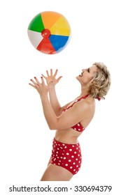 Portrait Of A Beautiful Mid 30s Woman Dressed In Vintage Retro Polka Dot Bikini Throwing A Beach Ball In The Air Isolated On White