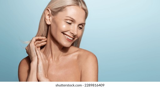 Portrait of beautiful mid 50s woman, senior model with perfect skin glow, smiling with eyes closed, posing for skincare product advertisement, blue background. - Powered by Shutterstock