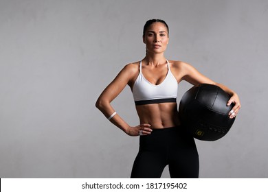 Portrait of beautiful mid adult woman looking at camera while holding heavy medicine ball isolated on grey background. Strong woman holding sports ball after cross training workout with copy space. - Powered by Shutterstock