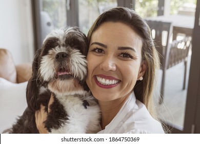 Portrait of beautiful middle age Brazilian woman and her pet dog at home looking at camera at home, making vedio call, recording vlog, women's day concept - Powered by Shutterstock