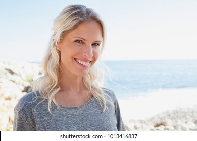 Portrait of beautiful middle age healthy woman visiting a rocky beach on sunny holiday vacation trip, looking smiling, outdoors. Mature female joyful expression, active recreation leisure lifestyle. - Powered by Shutterstock